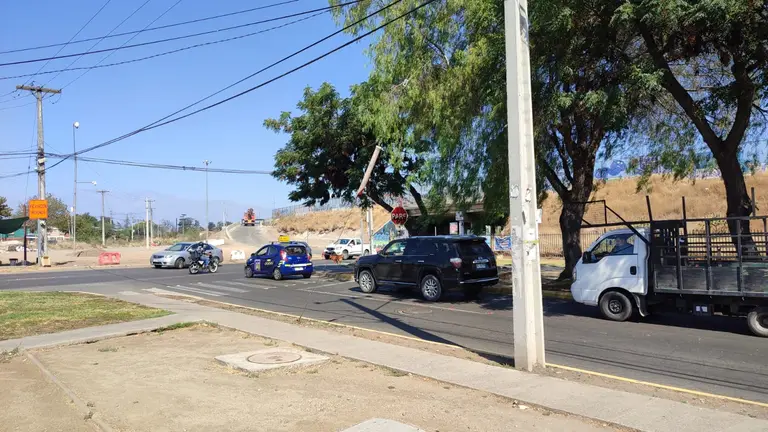 Tráfico en intersección con semáforo colgante y árboles.