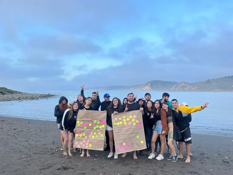 Grupo de amigos disfrutando en la playa con cartel.