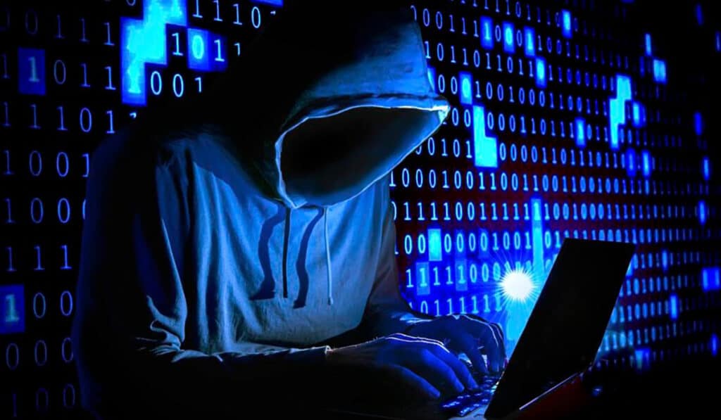 Hacker con capucha frente a pantalla con dígitos binarios.