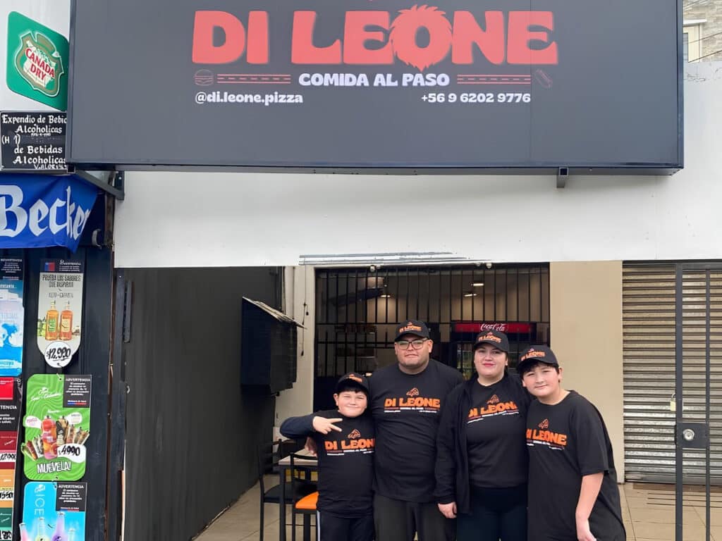 Familia de Di Leone Pizza con poleras y jockeys del local, frente a la fachada en avenida 4 Poniente, Maipú.