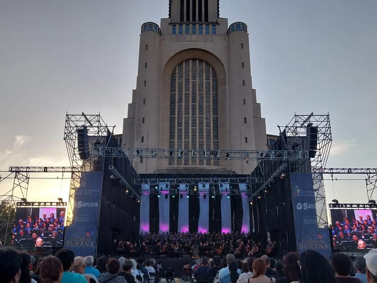 Concierto al aire libre, orquesta y público al atardecer.