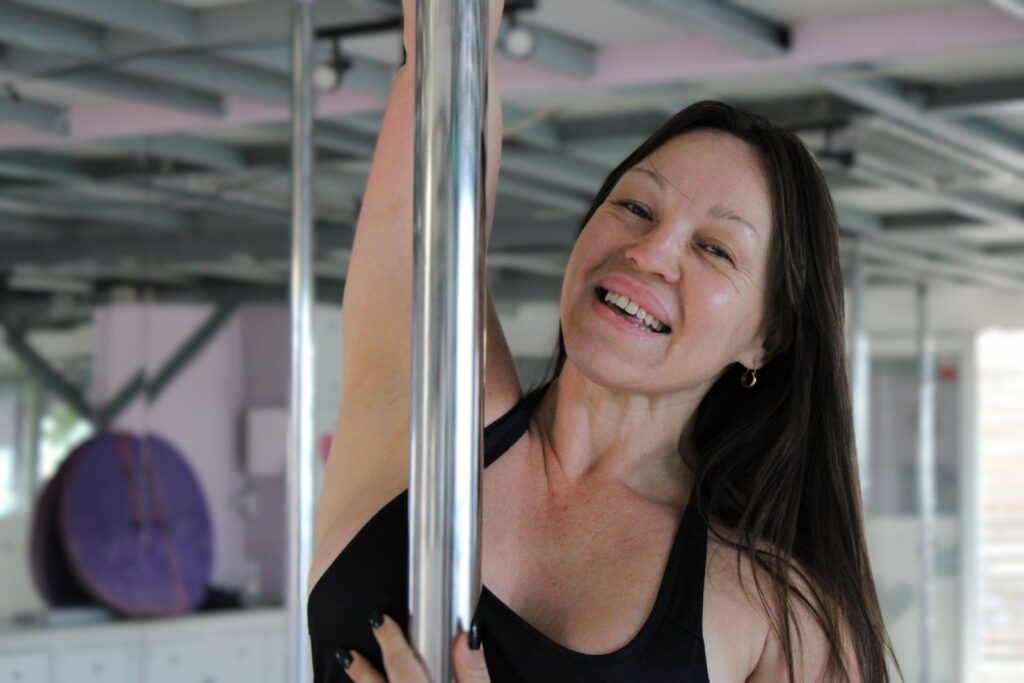 Mujer sonriente practicando pole dance en gimnasio